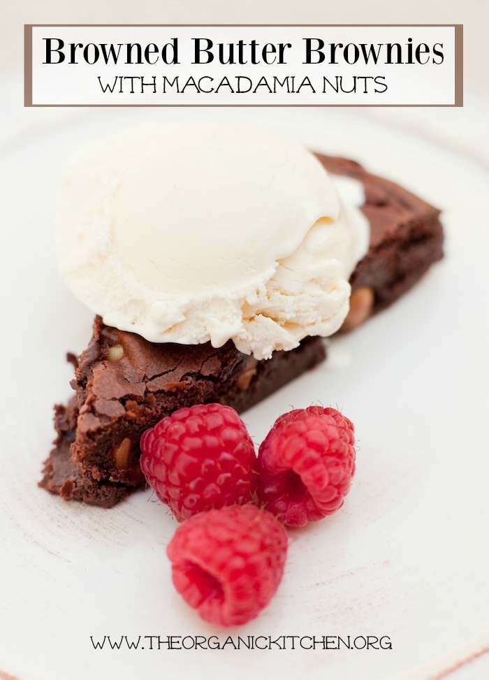 Browned Butter Brownies with Macadamia Nuts topped with ice cream and raspberries on a white surface