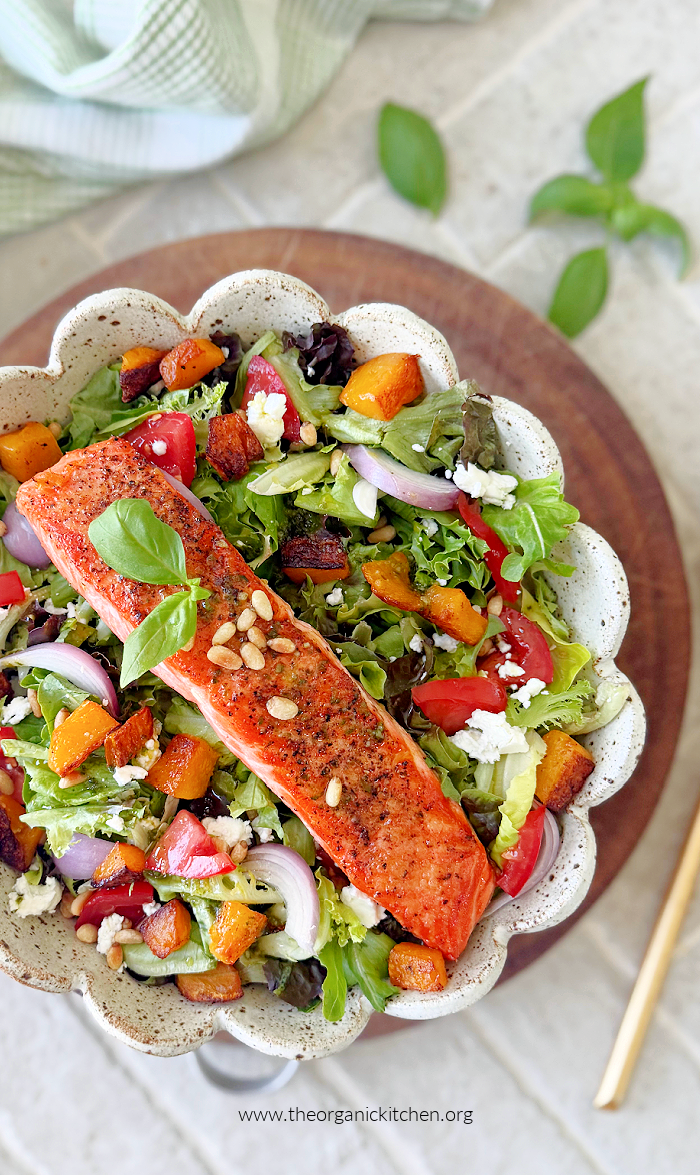 Fresh and Easy Basil Vinaigrette Salmon Salad with Easy Basil Vinaigrette on white plate set on wood cutting board surrounded by basil leaves