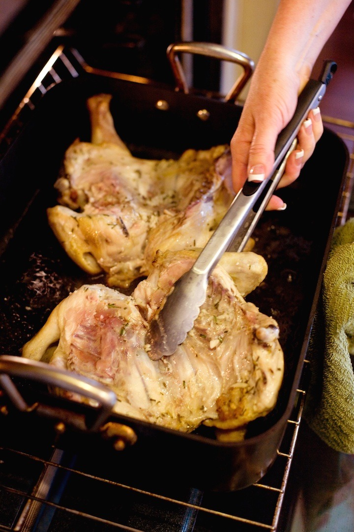 Chicken al Mattone in a roasting pan being turned with tongs