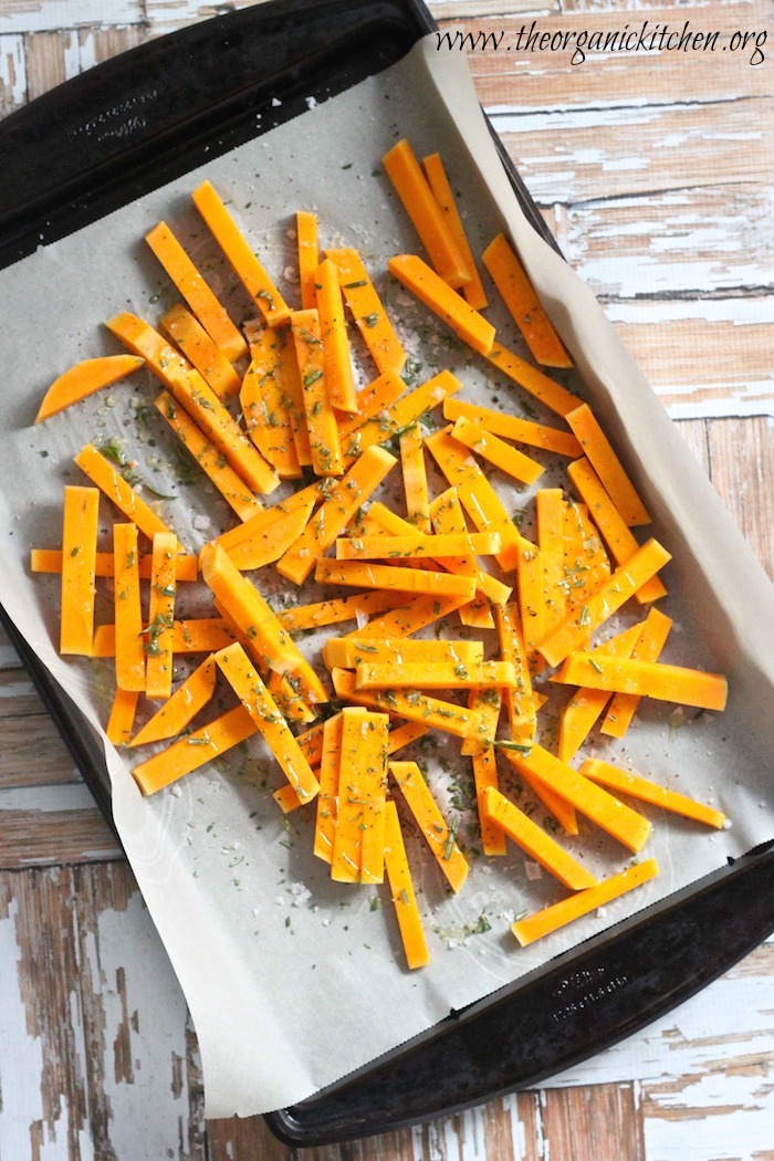 Butternut squash cut into fries on parchment paper covered cookie sheet 