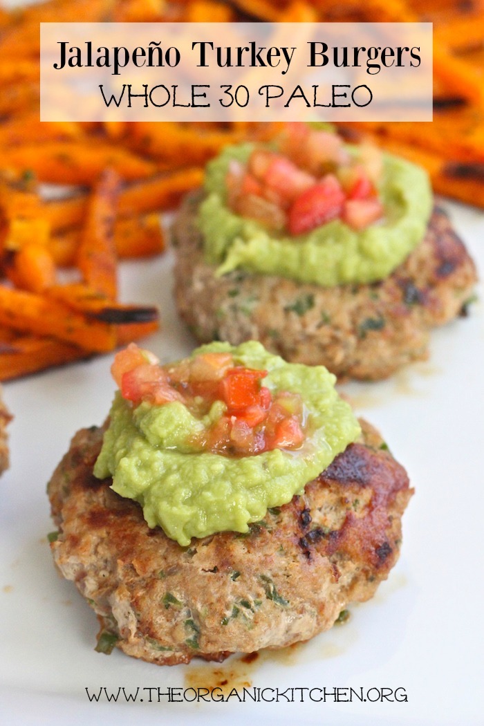 Two Jalapeño Turkey Burgers topped with guacamole and pico de gallo on a white plate with roasted butternut squash "fries" in the background