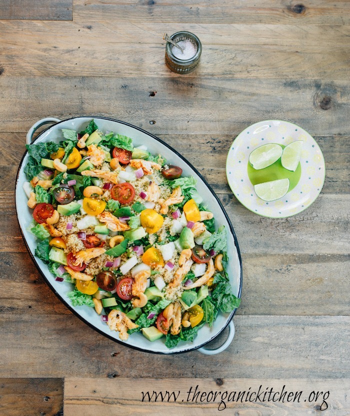 A platter of Easy Blackened Chicken and Quinoa Salad on a wooden table with a small bowl of sea salt and a saucer of lime wedges