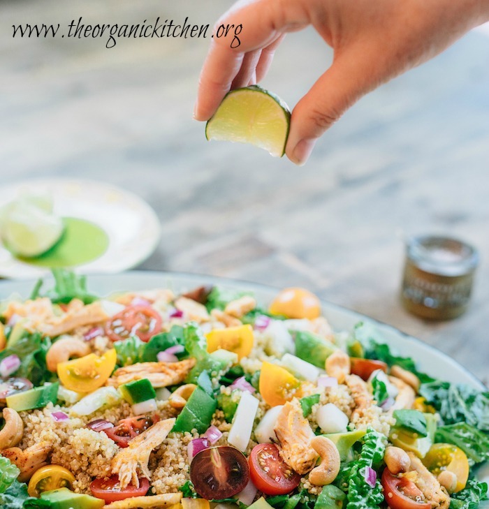 A woman's hand squeezing a lime wedge onto the Easy Blackened Chicken and Quinoa Salad