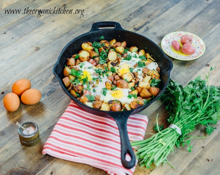 Crispy One Pan Potatoes with Eggs in a cast iron skillet surrounded by eggs, sea salt, and fresh herbs