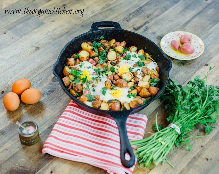 Crispy One Pan Potatoes with Eggs in a cast iron skillet surrounded by eggs, sea salt, and fresh herbs