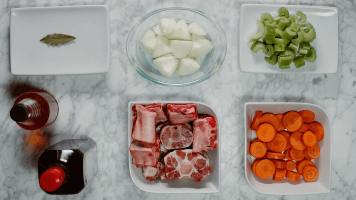 Bowls filled with the ingredients to make bone broth:beef, carrots, celery, onion, and bay leaf