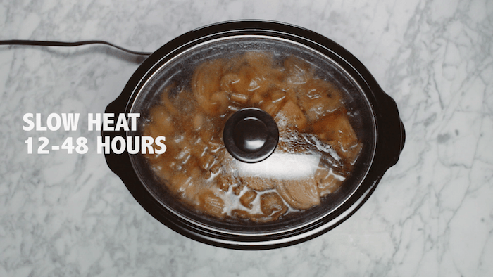 A lidded crock pot with bone broth in it on gray and white marble counter