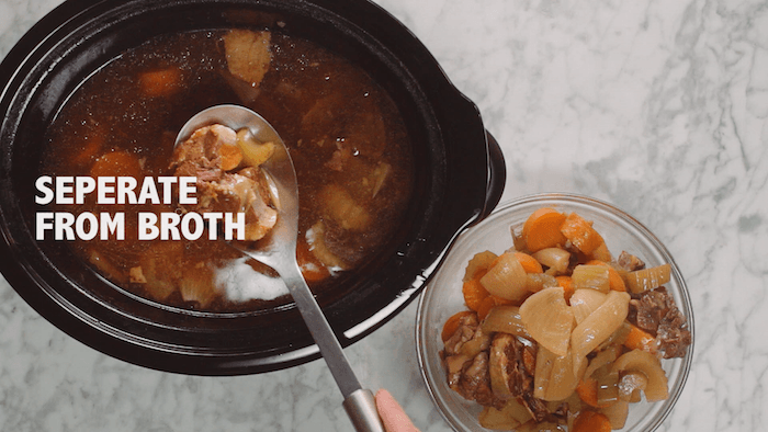A spoon filtering out vegetables from a  crock pot filled with bone broth