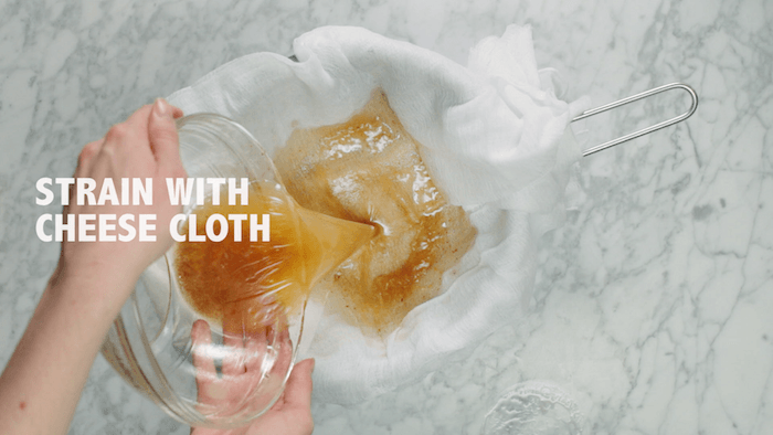 A woman's hand pouring bone broth through cheesecloth into a bowl 