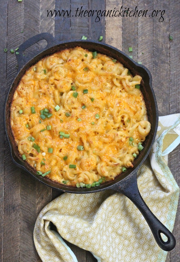 A black cast iron pan filled with Old Fashioned Skillet Macaroni and Cheese set on a wooden table with a yellow dish towel 