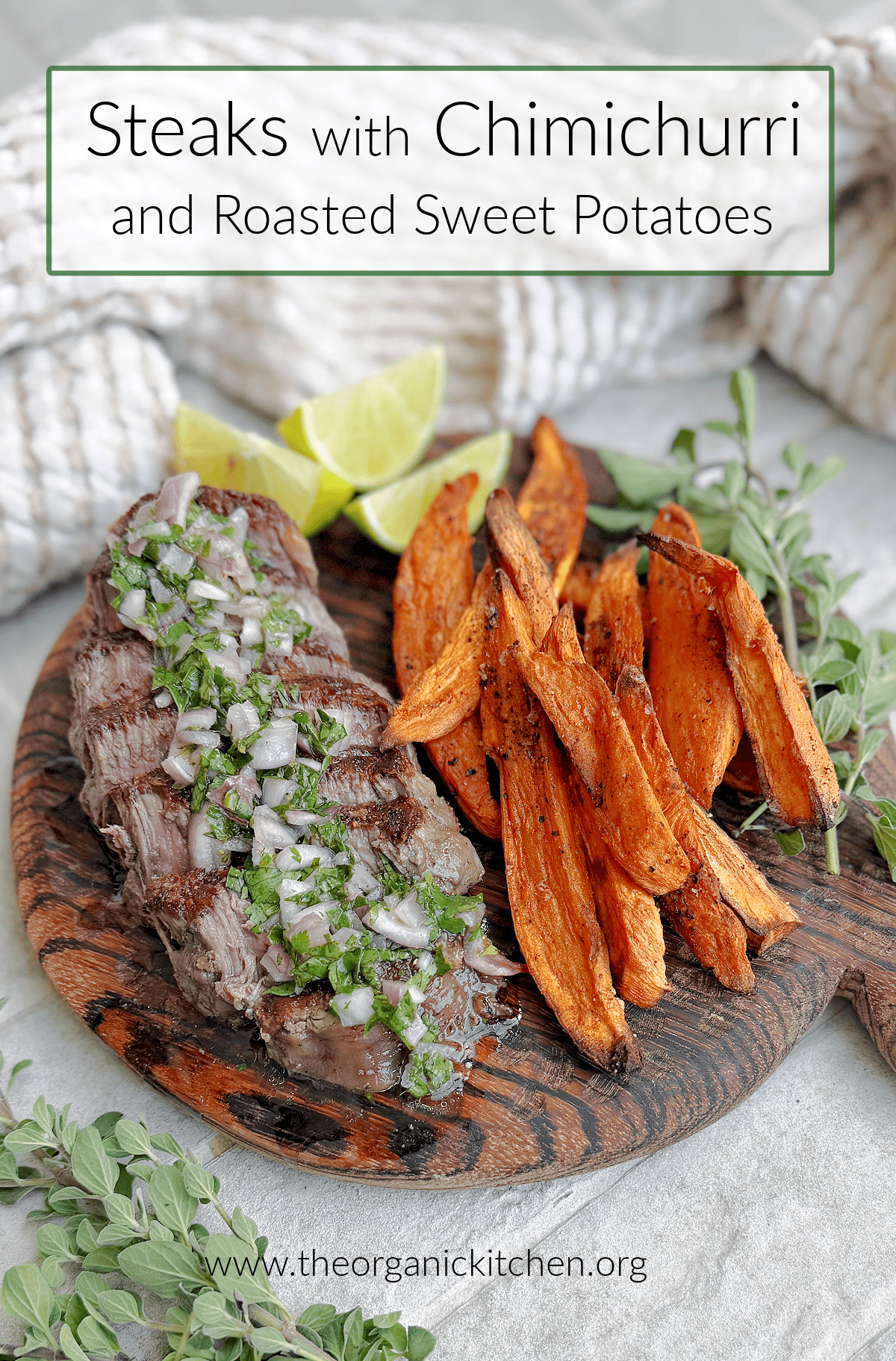 Steaks with Chimichurri and Roasted Harissa Sweet Potatoes on brown wood cutting board surrounded by herbs and lime wedges