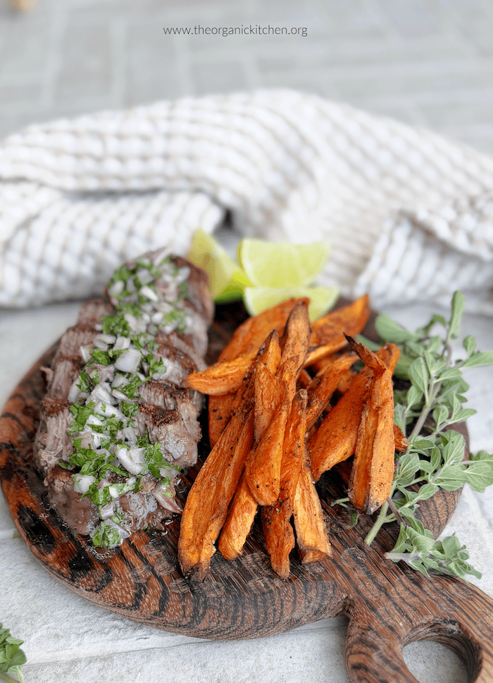 Steaks with Chimichurri and Roasted Harissa Sweet Potatoes on cutting board with beige and white dish towel in background