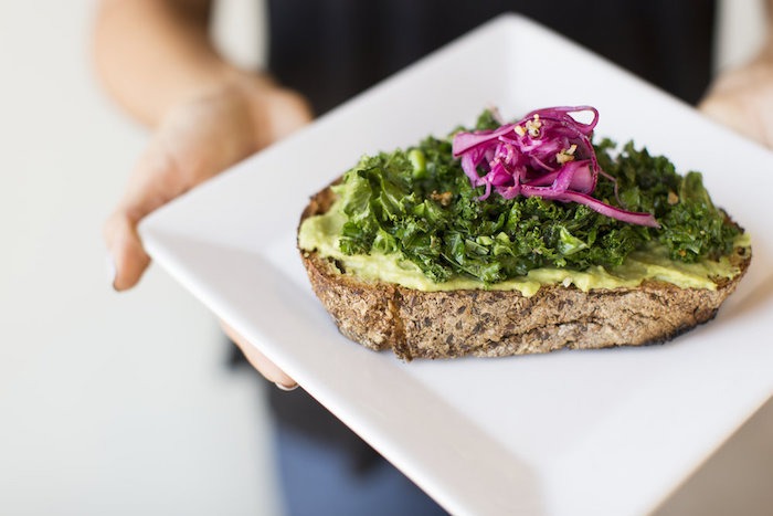 Kale Avocado Toast on white plate held by a female