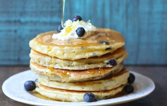 A white plate with Blueberry Lemon Ricotta Pancakes and maple syrup