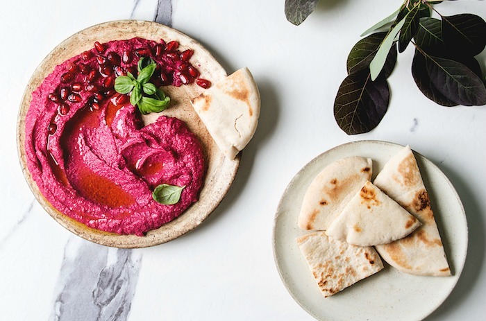 Bright pink better ummus on plate with pita bread triangles