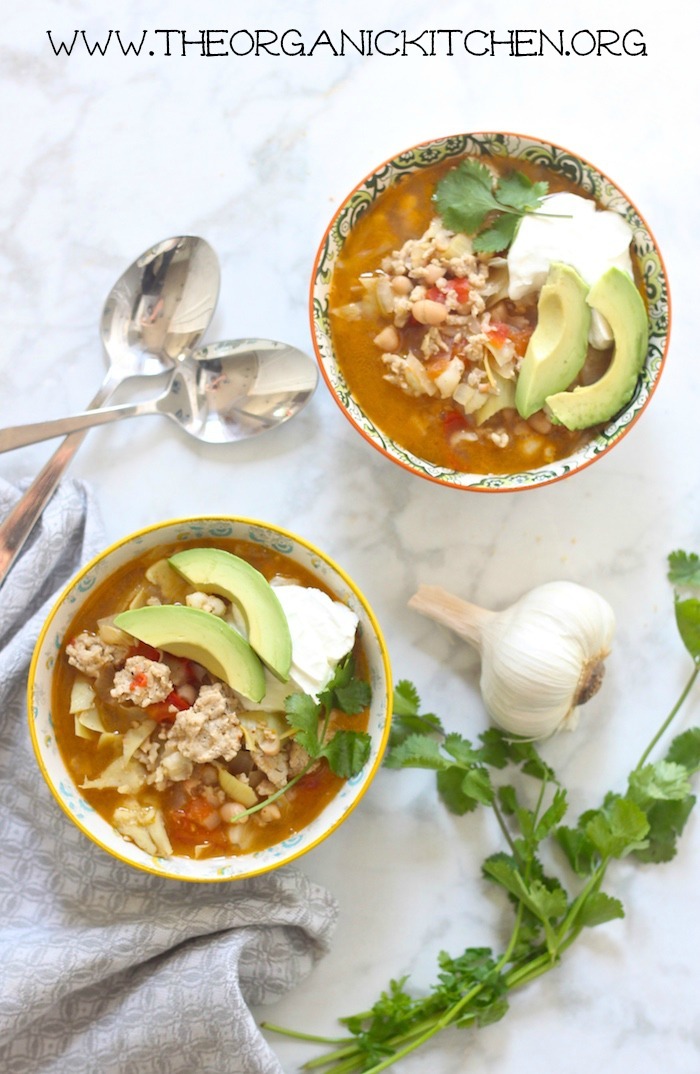 Flat lay of two bowls of Chicken Chili garnished with sour cream, avocados and cilantro on white marble surface