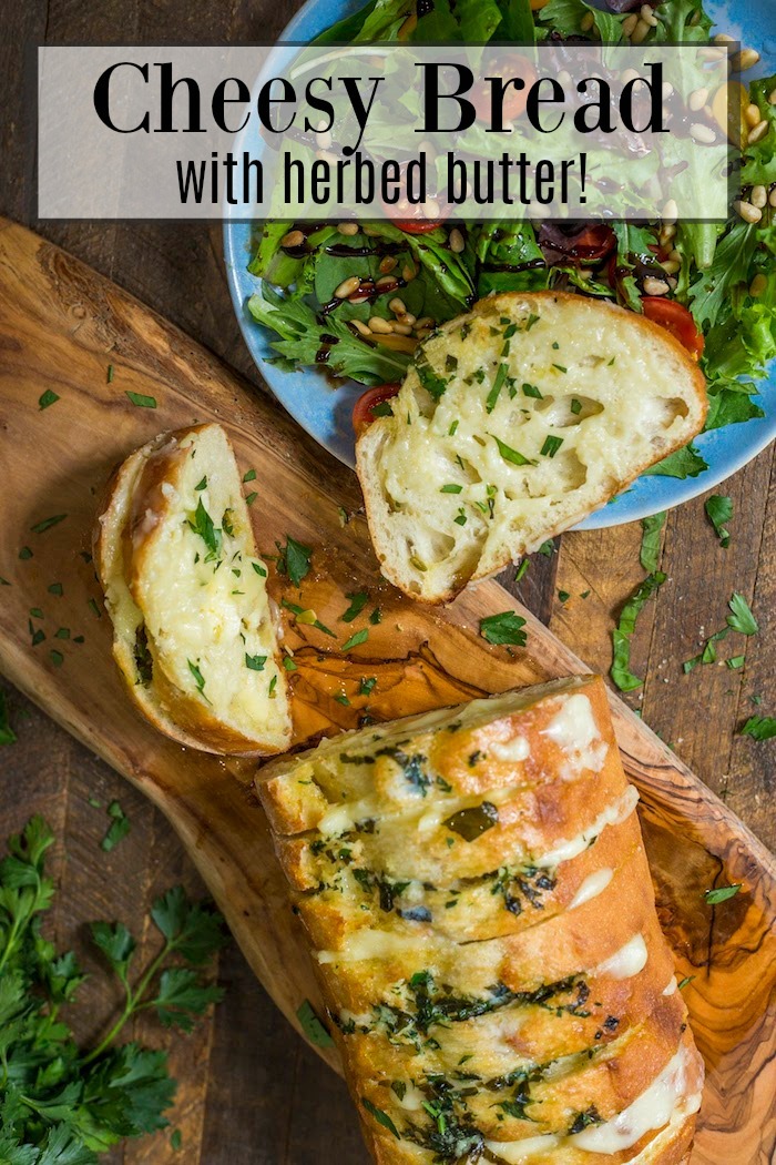 Cheesy Bread with Herbed Butter on a wood cutting board with a salad in blue bowl