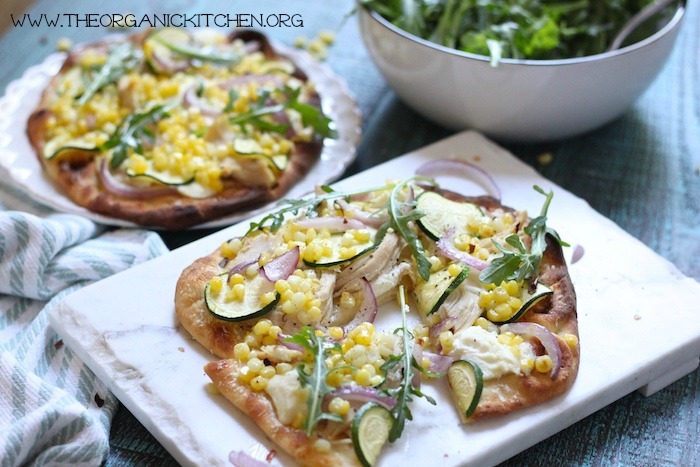 Two Easy Zucchini & Corn Grilled Naan Pizza on white plates with a bowl of salad in the background