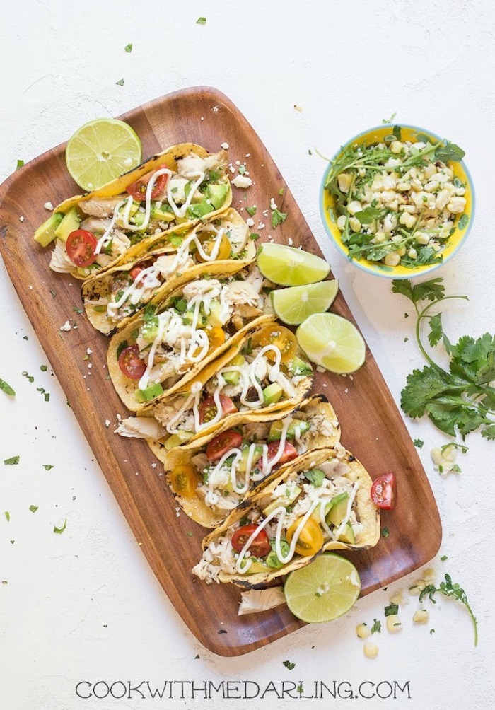 Six chicken tacos with lime crema on a wooden plate as part of 50+ Taco, Tostada and Fajita Recipes!