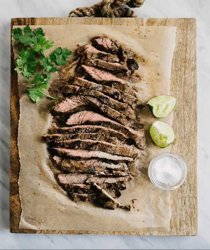 Sliced beef with cilantro and lime wedges on a wooden plate as part of 50+ Taco, Tostada and Fajita Recipes!