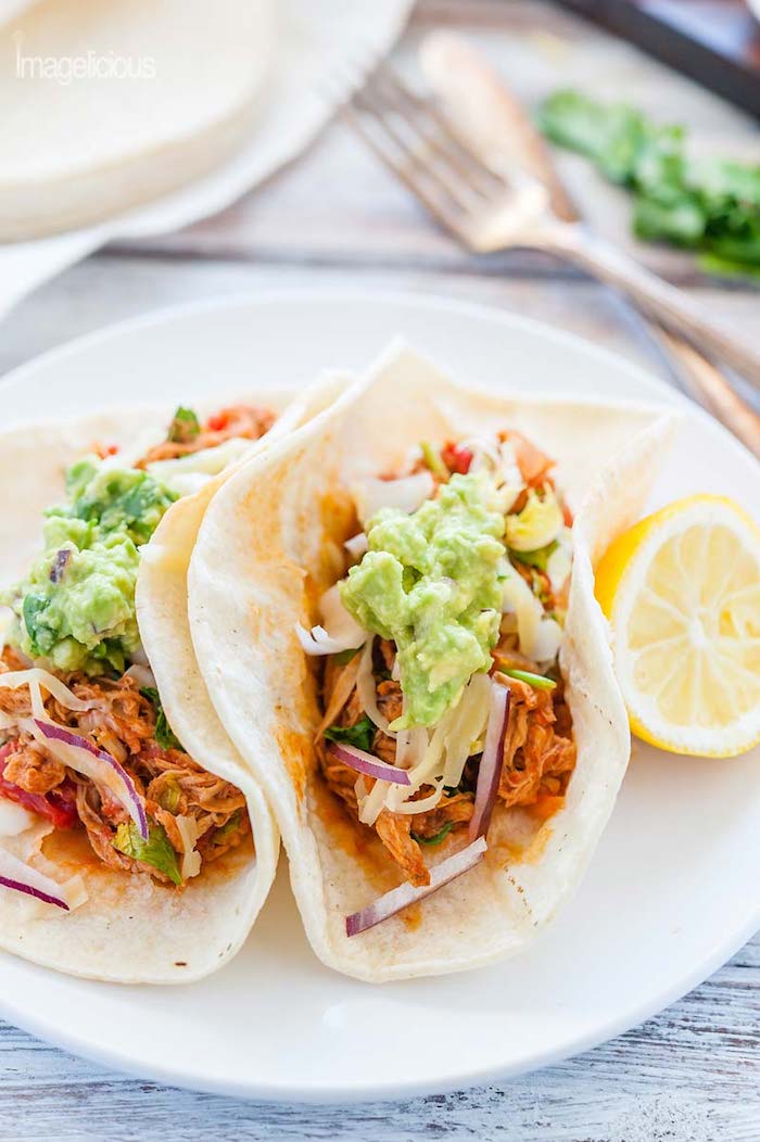 Two chicken tacos with guacamole and a lemon wedge on white plate as part of 50+ Taco, Tostada and Fajita Recipes!