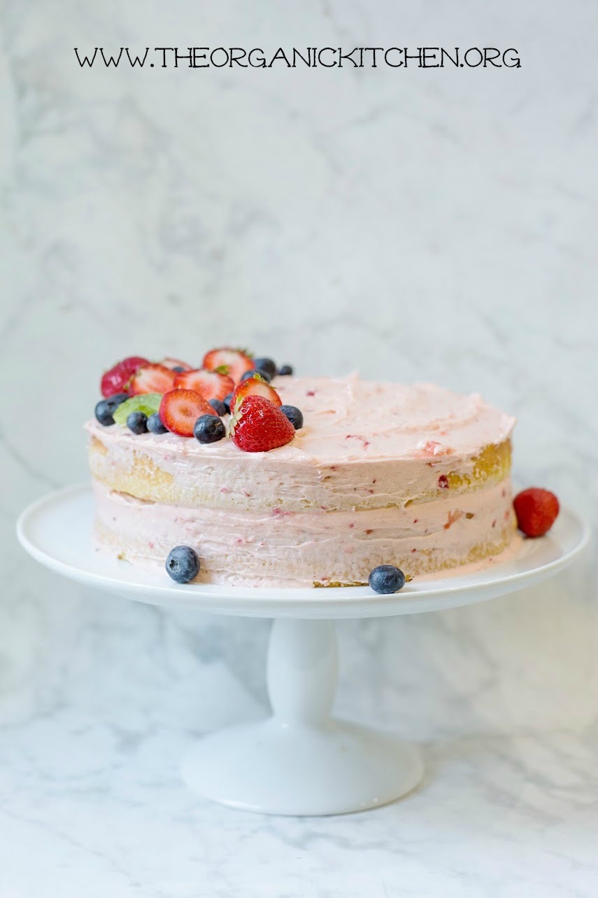 Vanilla Buttermilk Cake with Strawberry Buttercream Frosting on a white cake plate set in front of a marble backdrop