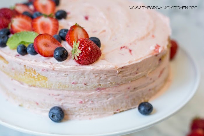 Vanilla Buttermilk Cake with Strawberry Buttercream Frosting topped with berries set on a white cake plate