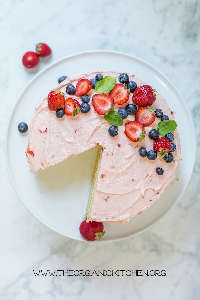 A pink topped with berries cake with a slice cut out set on a white plate