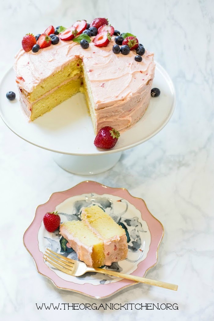 Vanilla Buttermilk Cake with Strawberry Buttercream Frosting with a slice removed on pink and white plates