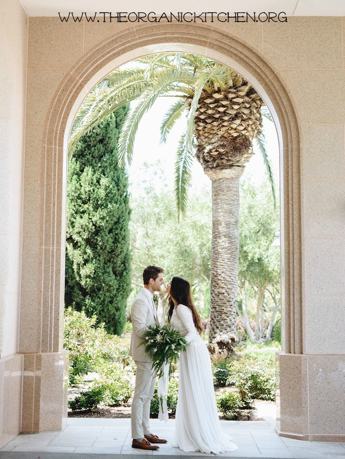 A bride and groom standing under an arch with a palm tree in the background