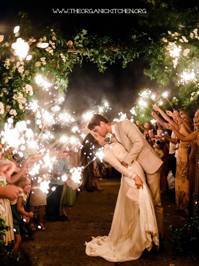 A grrom bending his bride back and kissing her while wedding guests hold sparklers