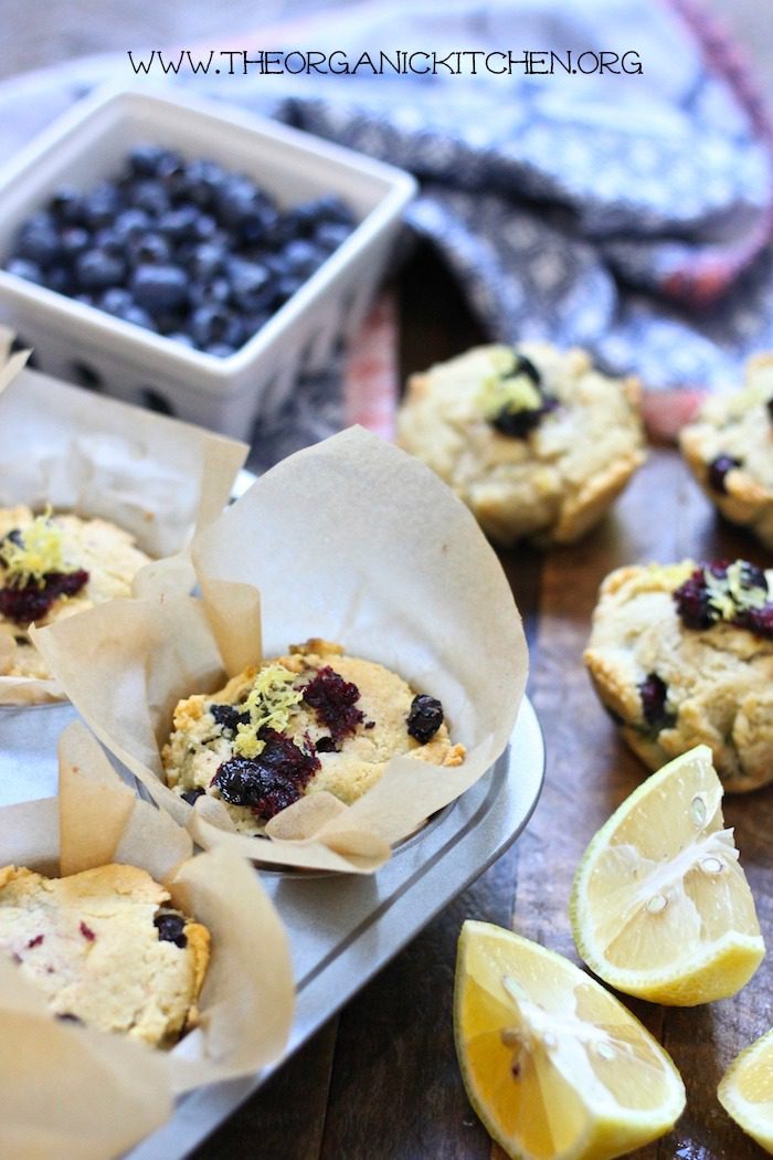 Keto Lemon Blueberry Muffins in muffin tin with blueberries and lemon wedges in foreground and background