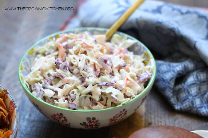 Coleslaw in a pretty bowl with gold serving spoon on wood table