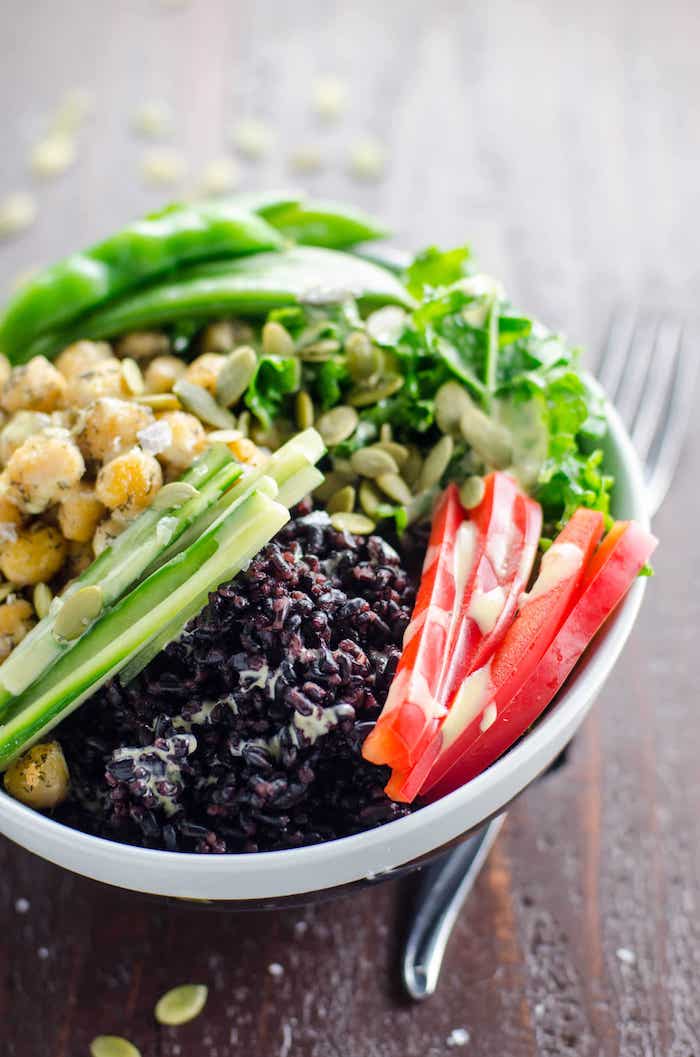 A white bowl over flowing with greens, chick peas, red peppers, and black rice as part of 12 Fantastic Rice Bowl Recipes!