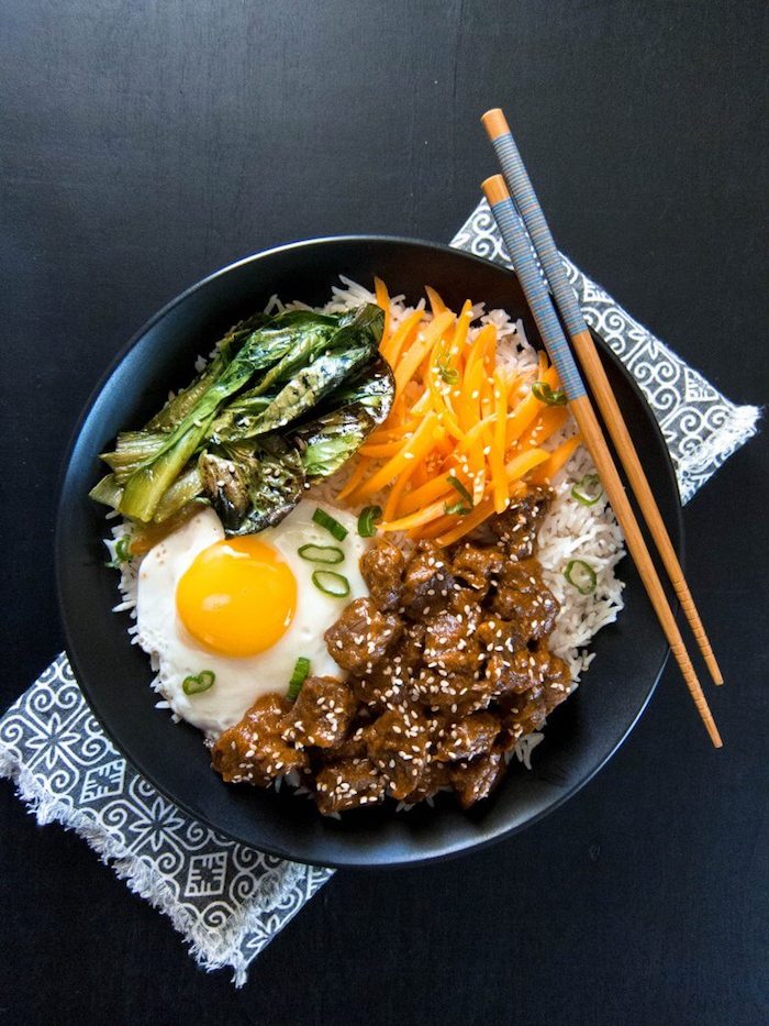 A black bowl of rice, beef, carrots, bok choy and fried eggs with chop sticks as part of 12 Fantastic Rice Bowl Recipes!