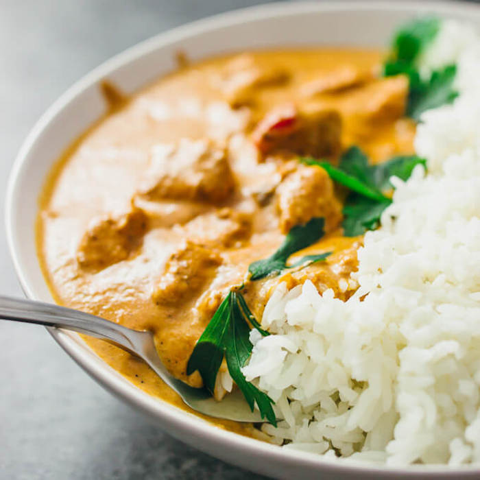 A white bowl with Chicken Tikka Masala, parsley, rice and a spoon on grey table as part of 12 Fantastic Rice Bowl Recipes!