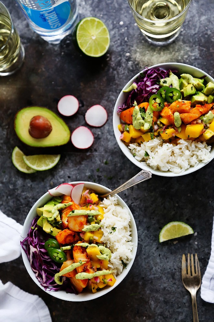 Two Fish Taco Rice bowls surrounded by avocados, limes, and drinks on grey table as part of 12 Fantastic Rice Bowl Recipes! 