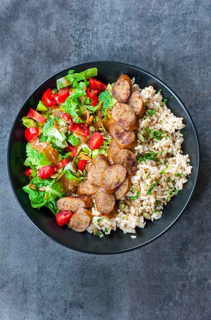 A blaack bowl filled with rice, sausage, green and red vegetables on black table as part of 12 Fantastic Rice Bowl Recipes!