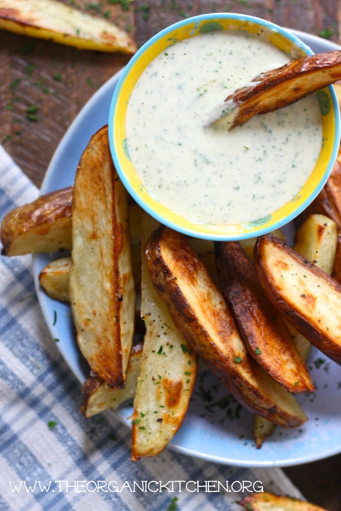 A blue plate loaded with baked potato wedges and a bowl of ranch dressing