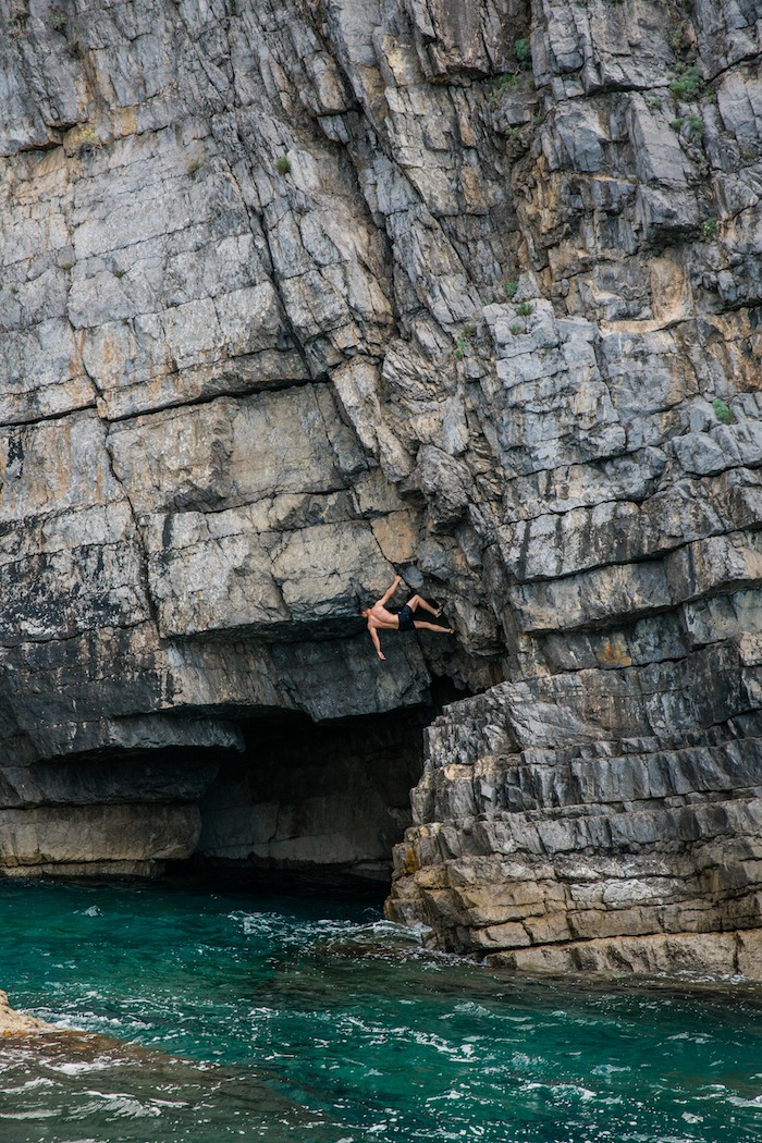 A young ma rock climbing above a cave in the sea of the Island of Capri