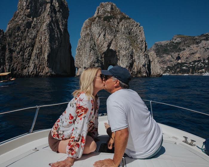 A couple on the bow of a boat kissing in front of the kissing arch by the island of Capri
