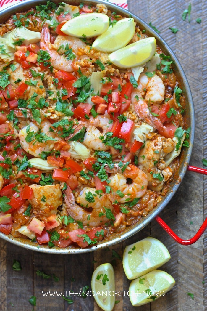 Paella Valenciana with Chicken, Chorizo and Shrimp in a paella pan surrounded by lemon wedges