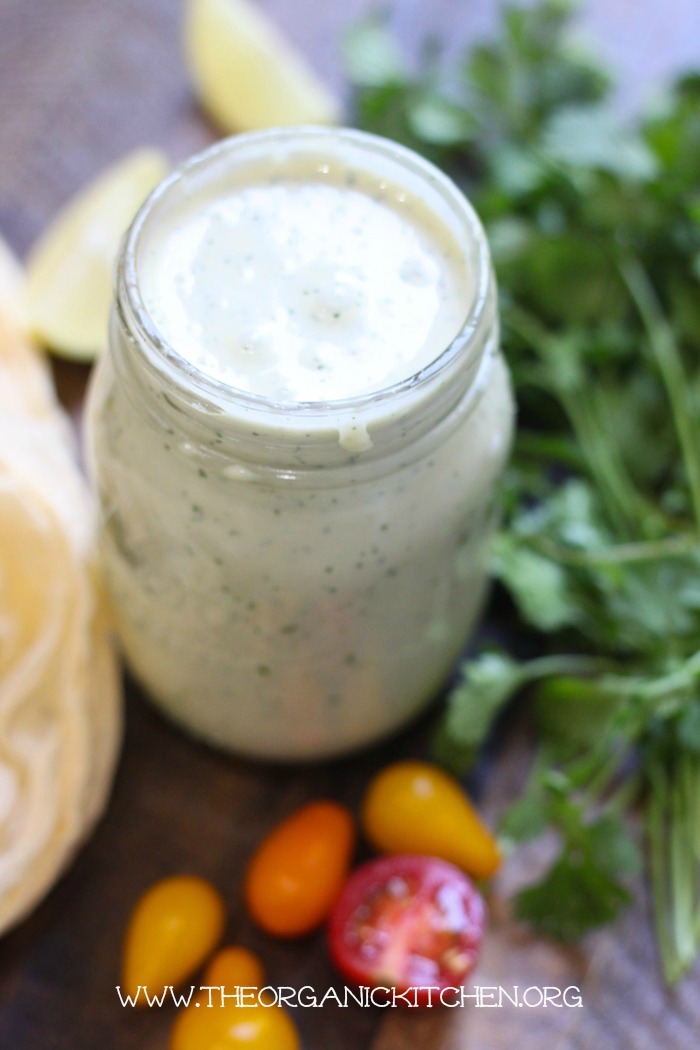 Homemade ranch dressing surrounded by herbs and tomatoes