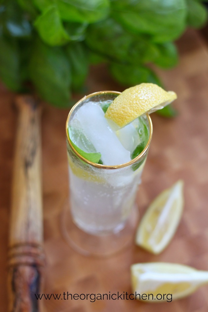 A clear glass with gold rim filled Lemon Basil Spritzer~ Non Alcoholic "Mocktail" garnished with lemon and basil