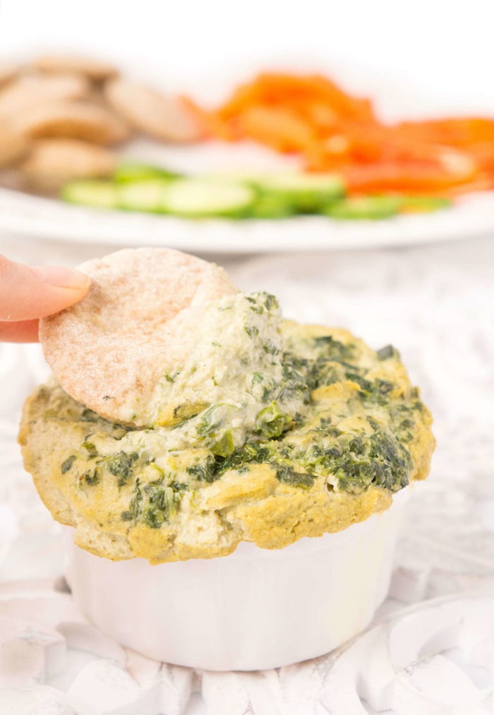 Fingers dipping a cracker into a ramekin of spinach artichoke dip as part of 20+ Whole30 Dips, Sauces and Salad Dressings