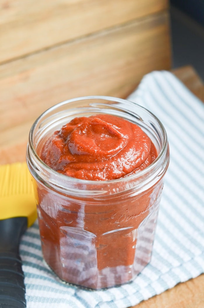 BBQ sauce in clear jar on stripped dish towel as part of 20+ Whole30 Dips, Sauces and Salad Dressings!