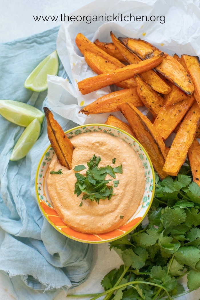 Easy Baked Sweet Potato Wedges with Chipotle Cashew Dip on white parchment and garnished with cilantro