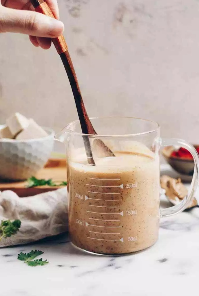 A jar of peanut sauce being stir with a wooden spoon as part of 20+ Whole30 Dips, Sauces and Salad Dressings! 