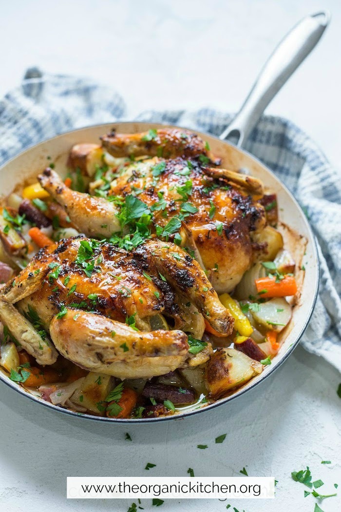 Roasted Citrus Herb Game Hens with Vegetables in a pan on white surface