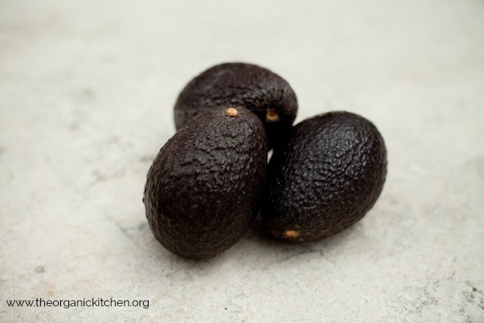 Three ripe avocados on a gray cement surface